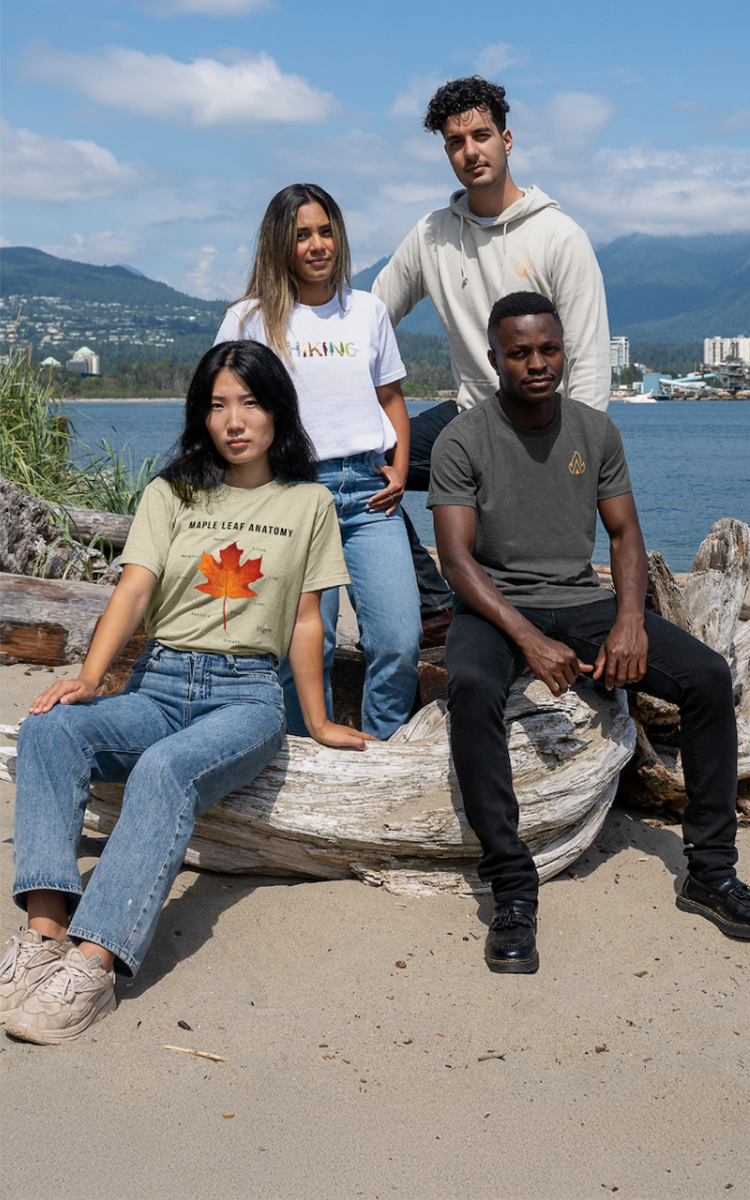 Group of diverse models wearing sustainable clothing with maple leaf design, sitting on a beach in Vancouver.