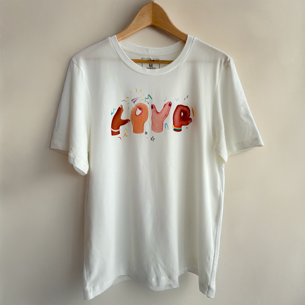 White sustainable t-shirt by VELU featuring the word “LOVE” formed by illustrated hands in diverse skin tones. Made in Canada from a soft lyocell and organic cotton blend.