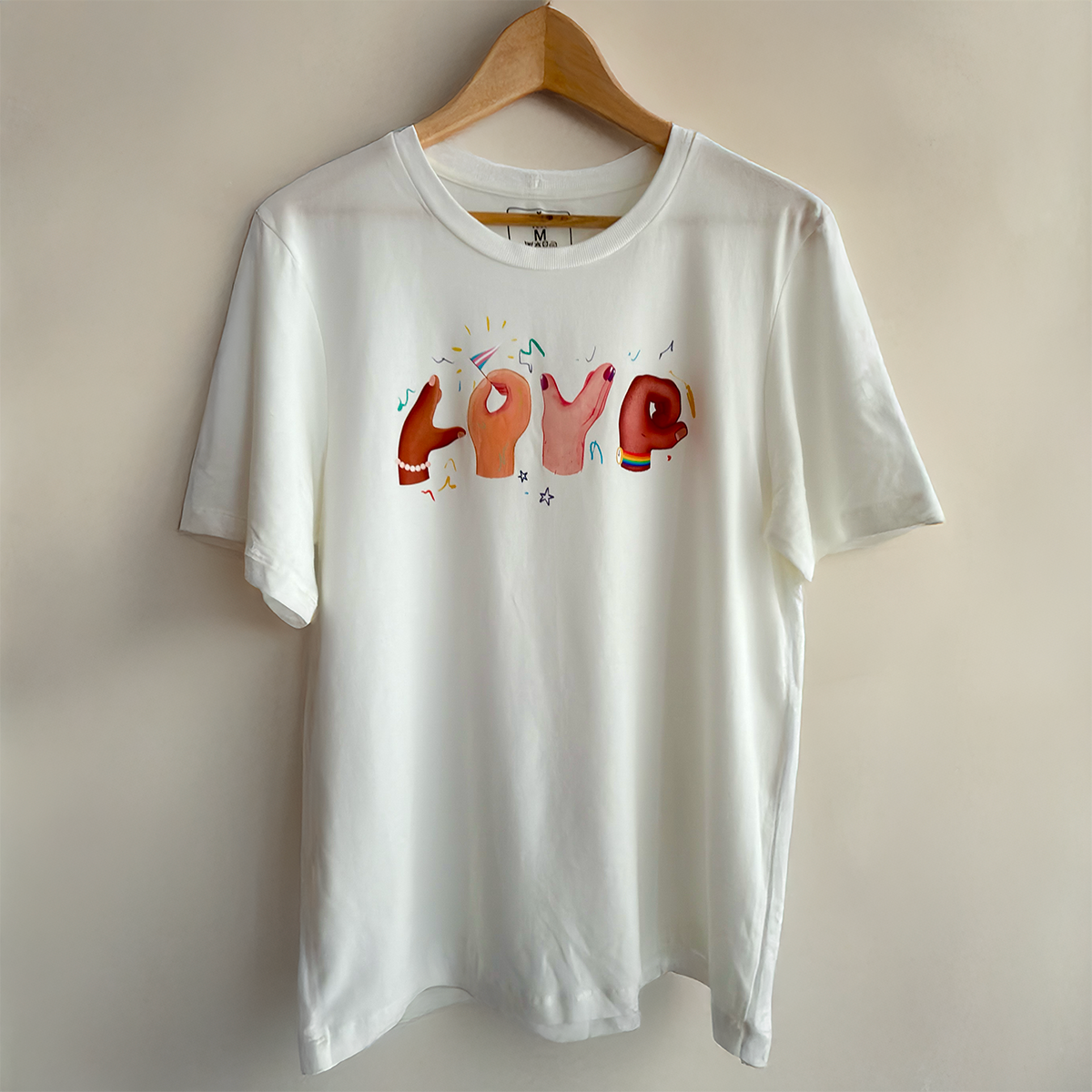 White sustainable t-shirt by VELU featuring the word “LOVE” formed by illustrated hands in diverse skin tones. Made in Canada from a soft lyocell and organic cotton blend.