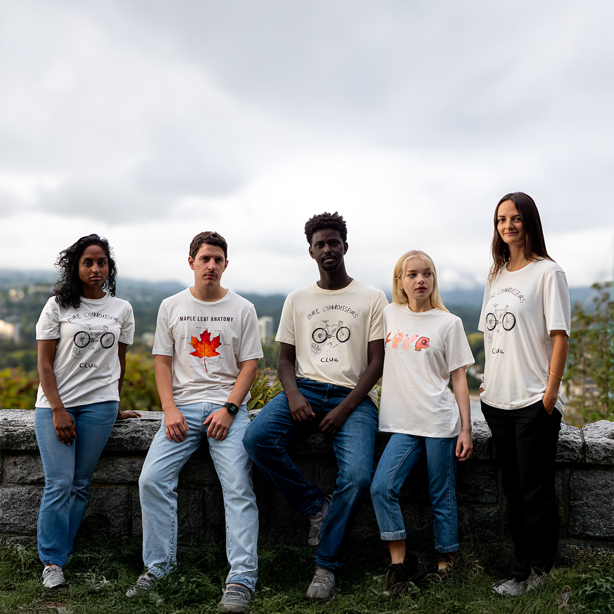 Group of five diverse models wearing VELU’s “Maple Leaf Anatomy,” “Love in Hands,” and “Bike Connoisseurs” T-shirts. Posing outdoors in Vancouver, showcasing locally made sustainable fashion.